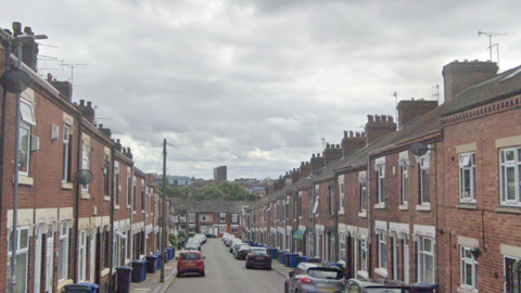 A street of terraced houses, with bins and cars outside many properties.