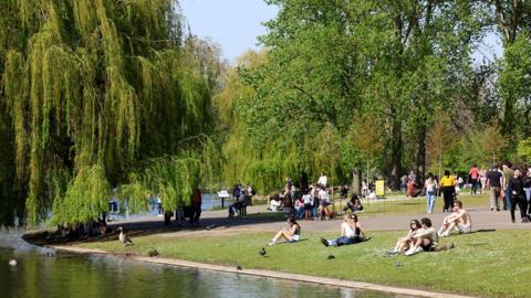 People sit on the edge of the boating lake in Regents Park, London on April 8, 2026 as warm, sunny weather arrived in the capital, with a high temperature forecast in the mid-20s. (Photo by Toby Shepheard / AFP via Getty Images)