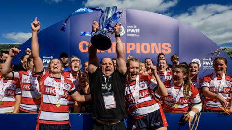 Sean Lynn (centre) holds the Premiership Women's Rugby trophy in the air surrounded by players after the club won the final last season