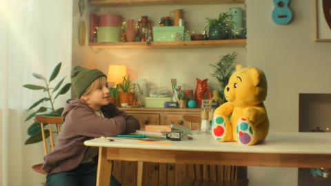 A child sits at the table with a plush Pudsey.