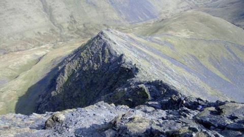 A picture taken from the top of Blencathra looking down at Sharp Edge. The ridge is surrounded by steep drops on either side and is very rocky.