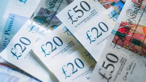 A photo showing a mixture of £20 and £50 notes lying on a table. 