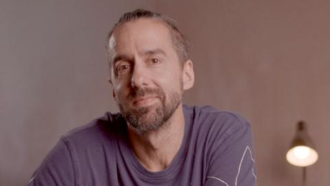 headshot of jamie bartlett, a man with black hair with grey at the temples, wearing a purple tshirt