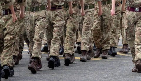 Legs, the identity of each person obscured, walk in a row with camouflaged trousers and black Army boots