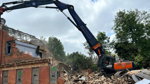 Demolition at the site with a machine pulling down walls