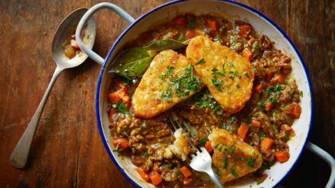 Top down view of a white bowl with mince and three hash browns in it, sitting on a brown table
