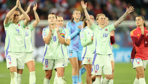 Wales players in lime green change kit applaud fans in St Gallen. Jess Fishlock is to the right with arms aloft and outstretched, Angharad James to her left applauds, and Kayleigh Barton is on the far left clapping above her head.