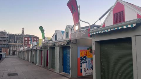 Norwich markets. A row of market stalls with coloured shutters which are closed.