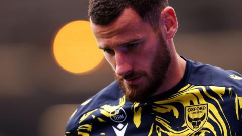 Elliott Moore wears a yellow and navy swirled pattern training top and looks down to the ground with a stern loook on his face.