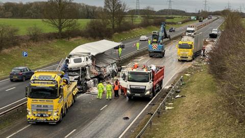 A clean-up operation takes place on the A19. A lorry has hit the middle barrier and debris is strewn across the road. A second lorry at the back also has its load spilled. There is a small National Highways lorry with staff in high-visibility clothing inspecting the area.
Some vehicles are travelling in the left southbound lane, with the rest of the road shut.