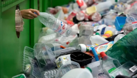 Hand dropping a plastic bottle into a recycling bin 