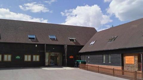 Children's nursery, Tigers in a L-shaped barn conversion. The building is dar brown wood with small windows on first floor and velux windows in its roof.