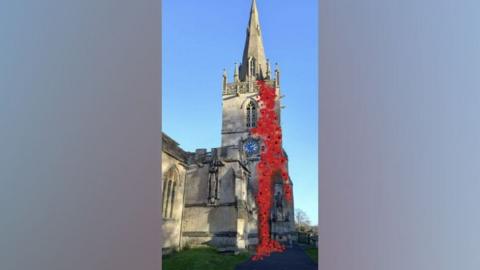 Church tower with short stone spire on top. The tower has a dark blue clock face with gold hands and numbers. An artist has altered the image to show a cascade of poppies draped from the top of the tower, down to the ground and the war memorial below.