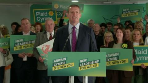 Rhun ap- Iorwerth in front of a crowd of people holding Plaid placards