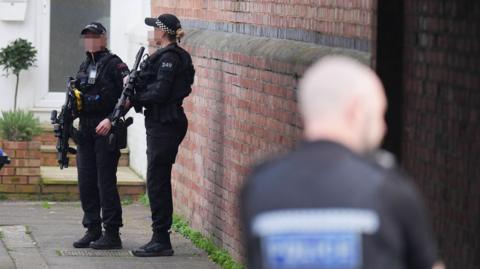 Two police officers with guns stood in a street. Their faces are blurred.