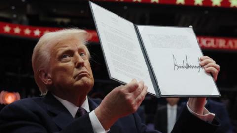 Donald Trump holds up an executive order after signing it