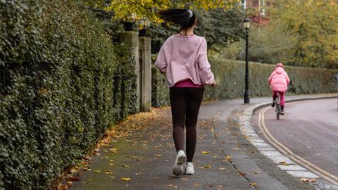 Female runner in Pink top and black leggings running on a pavement