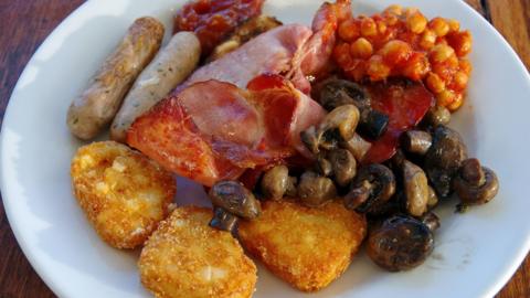 Cooked breakfast of fried bacon, sausages, hash browns, mushrooms, chickpeas in tomato sauce, toasted wholegrain bread and tomato chutney - stock photo