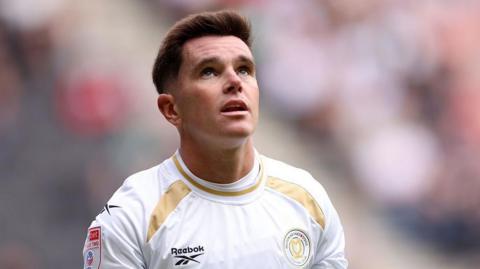 Liam Kelly in a white and gold MK Dons jersey during a match.