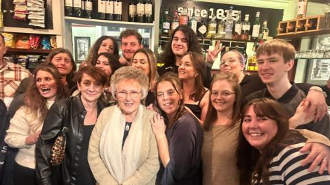 A large group of people old an young pose at a bar. 