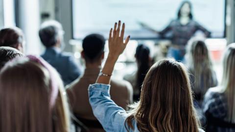 A woman at a presentation with her hand raised