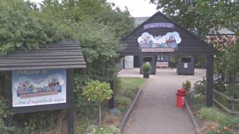 The entrance of Marsh Farm. There is a hut-like building that is accessible via a path. There is greenery next to the path and entrance