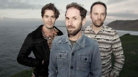The band standing on a cliff by the sea in the Gower Peninsula.