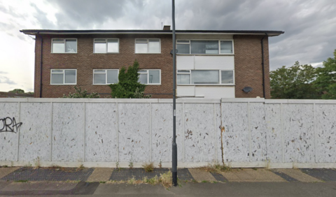 A three storey building, which used to be the police station, with wooden boarding around it. A lamppost is outside it, on a pavement in front of the building 