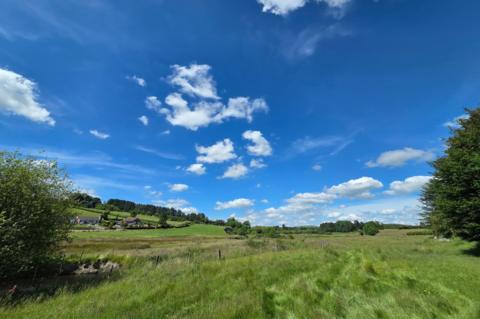 Green fields and rolling hills under a bright blue sky with scattered white clouds in St Harmon, Powys