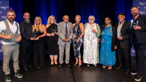 The winners - the group made up of 10 men and women - stand together on the stage, holding their awards 