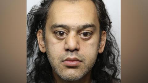 Asad Abbas, a man with shoulder-kength wavy black hair and brown eyes.