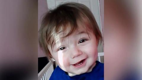 Ethan Ives-Griffiths, plentyn ifanc gyda gwallt brown a llygaid brown tywyll, yn hanner gwenu ar y camera. Mae'n edrych fel ei fod mewn crud ac yn gwisgo top glas.