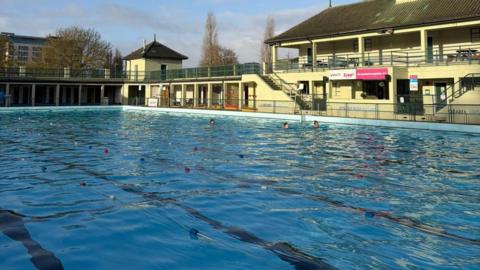 Large outdoor swimming pool with a two-storey green building in the background.