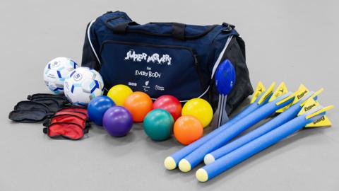 Sports equipment including a holdall, boccia kit, foam javelins and footballs.
