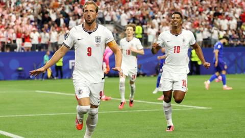 Harry Kane, England football player, celebrates after scoring a penalty for his team's first goal during the FIFA World Cup 2026 Group L match between England and Croatia at Dallas Stadium on June 17, 2026 in Arlington, Texas. Three players in England shirts are running forwards on a football pitch. 