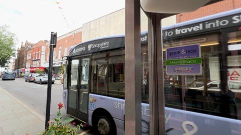 A violet coloured single decker bus at a bus stop in Shrewsbury