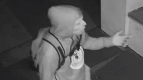 Black and white image showing a side profile of the suspect wearing a hoodie and backpack