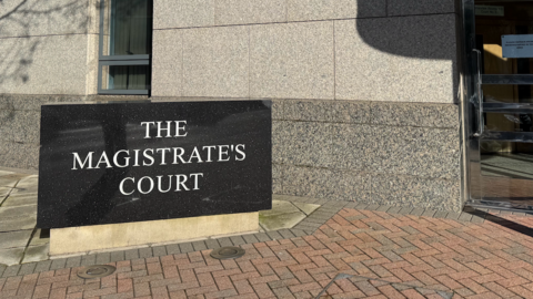 The Magistrate's Court sign outside a grey building and a revolving door to the right.