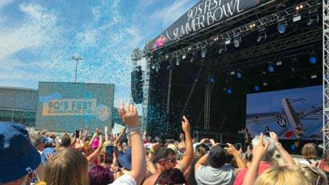 Festival goers with their hands up in front of a stage and a screen which reads 90's Fest Summer Bowl.