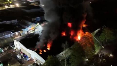 Aerial view of large recycling centre fire at night with flames and thick black smoke rising into the air