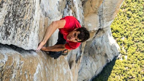 A man in a red shirt climbing up a rock wall
