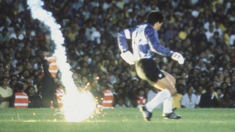 A footballer on a pitch with a flare behind them.