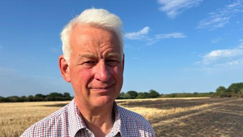 A head and shoulders picture of a man standing in a field. He is looking into the camera.