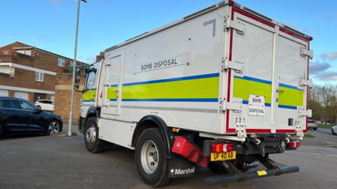 A white bomb disposal van with the reflective yellow and blue strip 