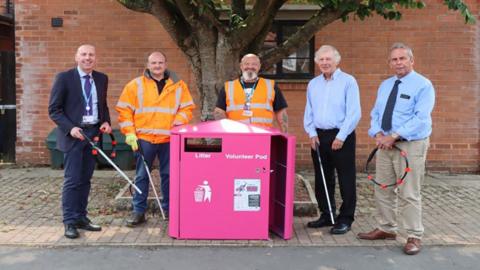 Five men, including council leader Rob Waltham, pose in front of a pink litter pod holding litter picking equipment