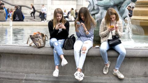 Teenage girls on smartphones in Trafalgar Square.