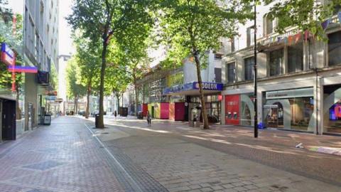 A view of New Street in Birmingham, showing trees along a paved shopping area, with an Odeon cinema sign on one side.