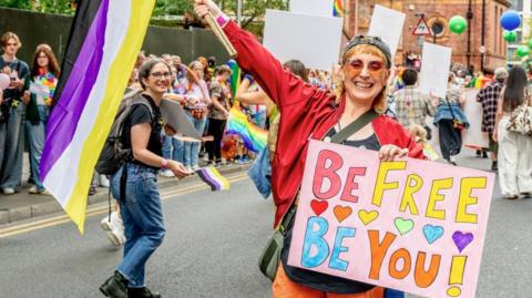 A woman is holding a colourful sign which reads: "Be Free Be You" as part of the Manchester Pride 2025 parade. 