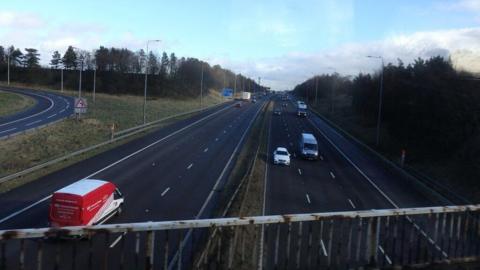 Motorway with three lanes on either side from the view of a bridge.