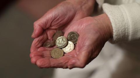A stock image showing a close-up of an elderly person's hands holding pound coins in their cupped hands.